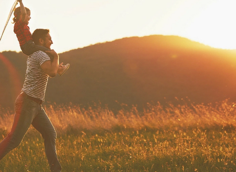 un homme porte un enfant sur ses épaules dans un champ au coucher du soleil