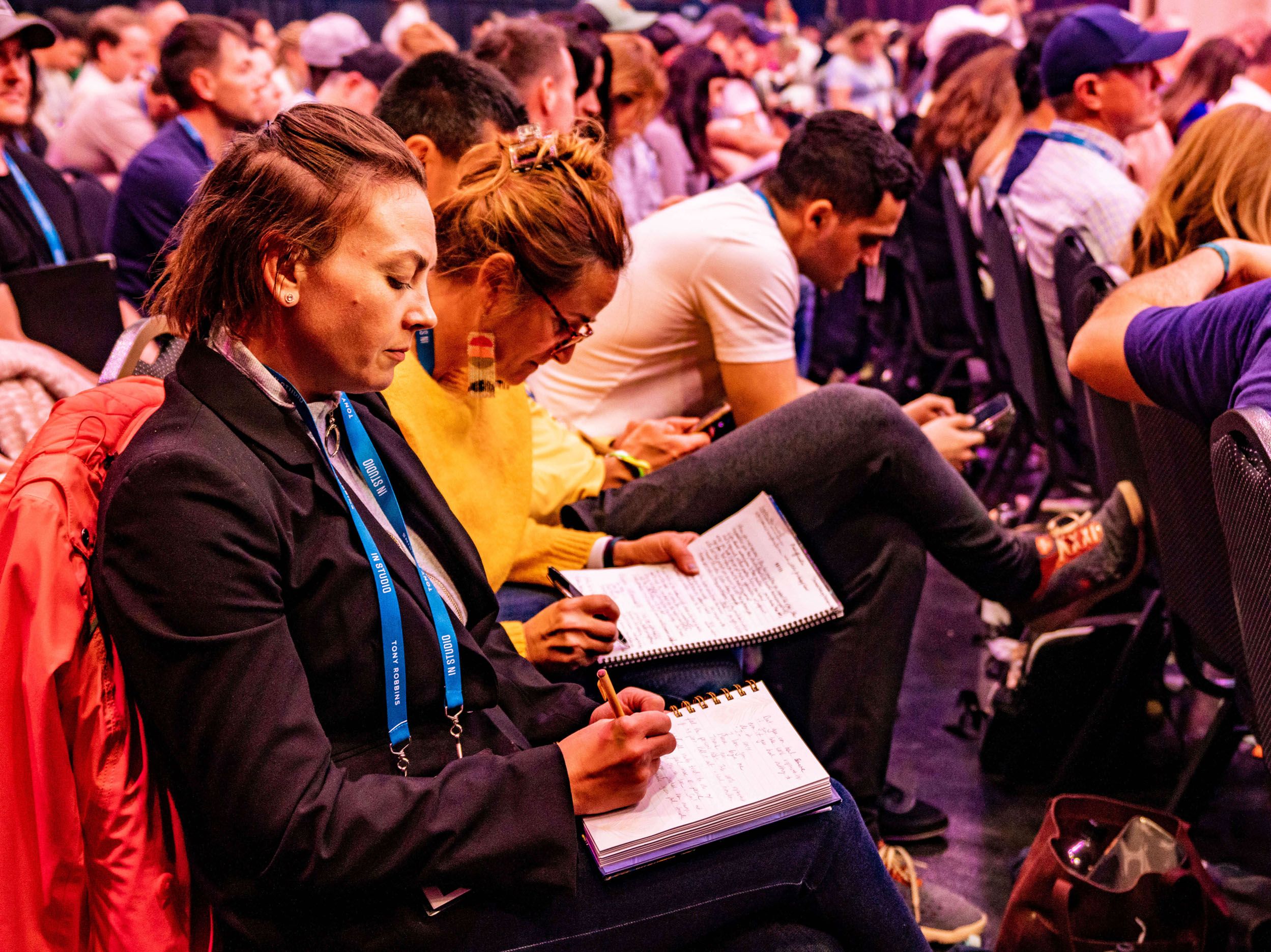un groupe de personnes sont assises dans un stade et prennent des notes dans des cahiers.